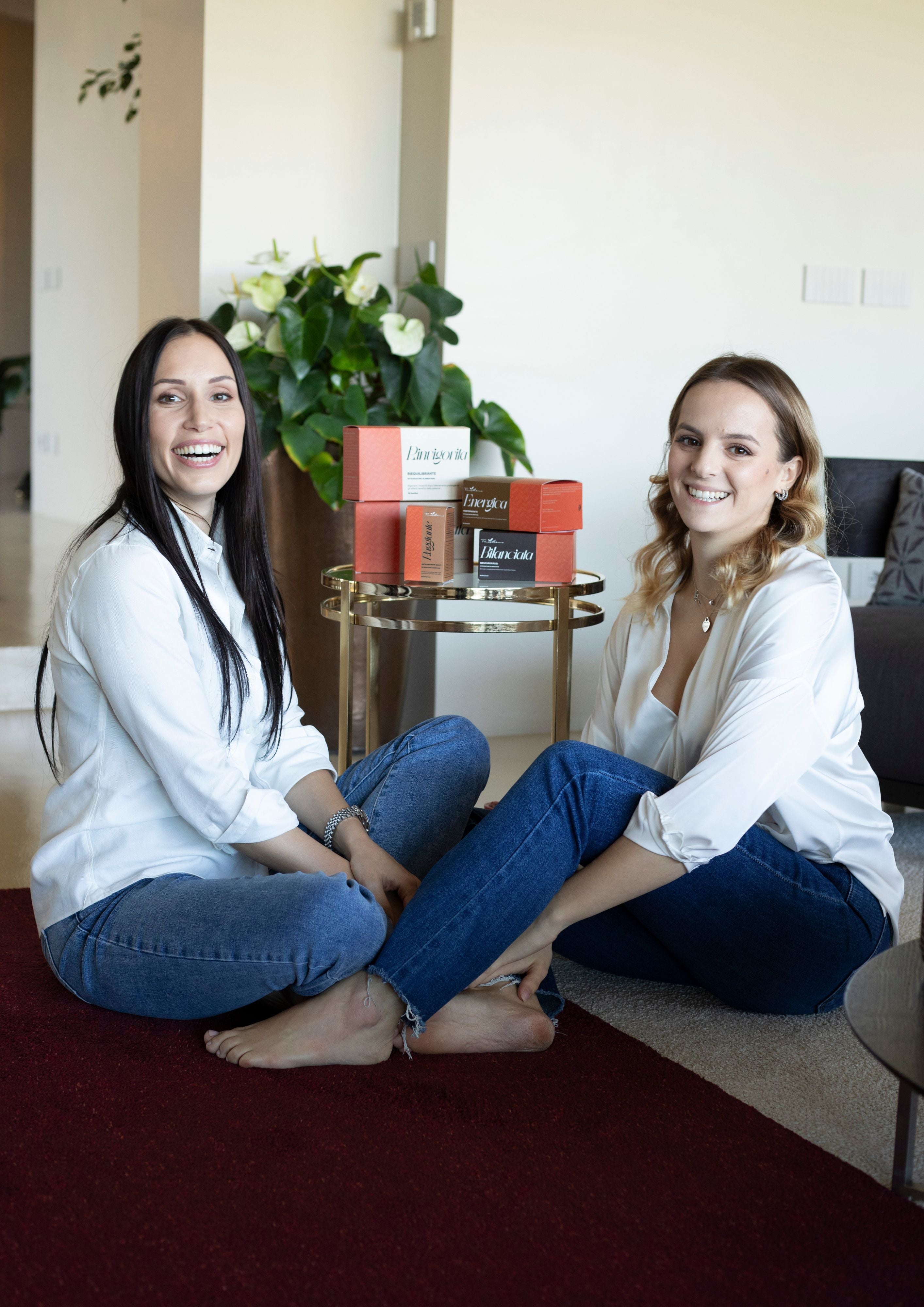 Ragazze sorridenti sedute sul tappeto con prodotti Toi Meme sul tavolino dietro di loro